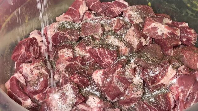 Raw pork cubes seasoned with black pepper and salt during meat marinating process for barbecue and homemade cooking preparation close up