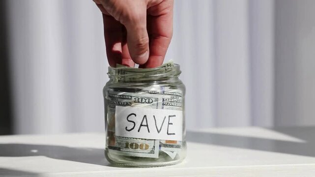 Person Adding Money to a Glass Savings Jar - Personal Finance and Investment Concept