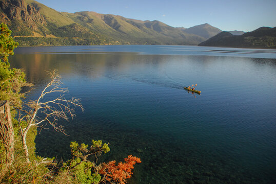 View of Nahuel Huapi Lake with two people in a yellow kayak on the calm blue water surrounded by high mountains in San Carlos de Bariloche, Rio Negro, Argentina.