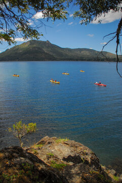 View of kayakers paddling on the blue waters of Nahuel Huapi Lake with distant mountains under a blue sky with light clouds San Carlos de Bariloche, Rio Negro, Argentina.