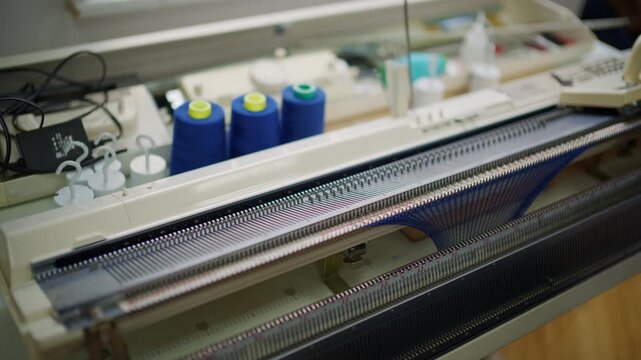 Close up of hands working with blue knitted fabric attached to a flatbed knitting machine