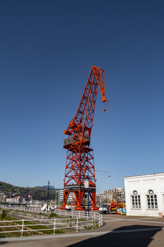 View of the historic red Carola Crane at the maritime museum dock under a clear blue sky in Greater Bilbao, Basque Country, Spain.