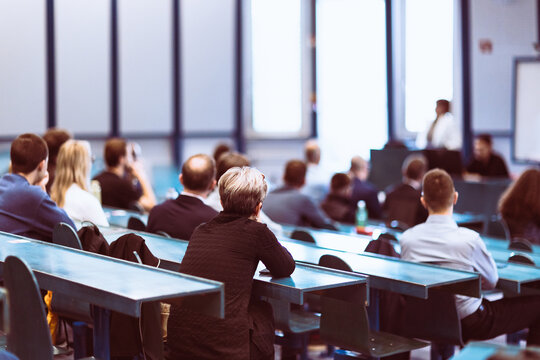 A large group of diverse people attending a professional presentation or educational workshop in a modern lecture hall. Focus on the audience from behind.
