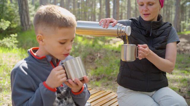 Mother pours hot tea. Family friendly camping drink from a stainless steel thermos. A boost of energy during long walks and mountain climbing.