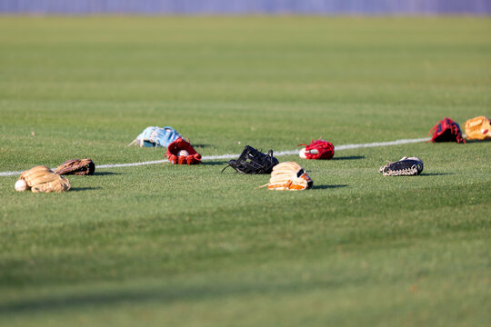 Multiple baseball gloves and baseballs rest on the grass beside a painted field line during pregame warmups at a high school baseball game in Olive Branch, Mississippi.