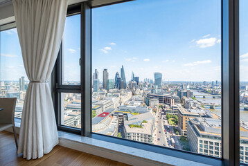 Fototapeta premium Bright city skyline view through a large modern window framed by a white linen curtain
