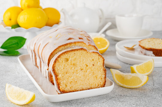 Lemon loaf cake with sugar icing on a white plate on a stone background. Copy space.
