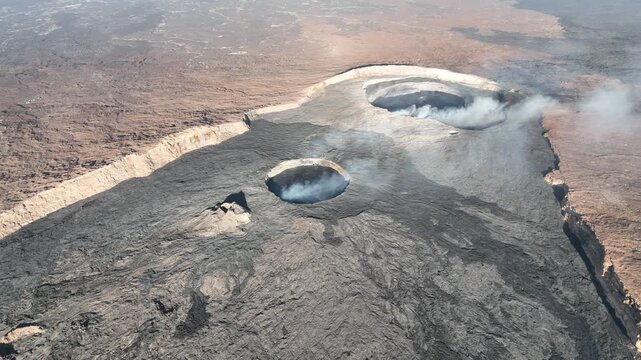 Aerial view of active volcanic craters with smoke rising from the dark basaltic lava fields in the Danakil Desert, Dallol, Afar, Ethiopia.