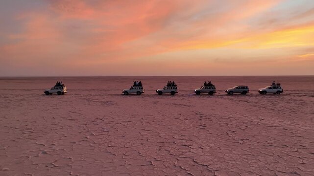 Aerial view of a convoy of off-road vehicles parked on the cracked salt flats of the Danakil Desert under a vibrant sunset sky in Dalol, Afar, Ethiopia.