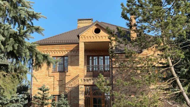 Yellow brick cottage under blue sky, sunlit balcony and chimney framed by pine trees, warm golden facade textures, tidy garden