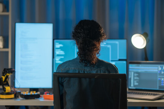 rear view of Asian woman codes late on multiple screens, building SaaS app, API integration, cloud DB sync, cybersecurity checks, wireless connection and team communication.

