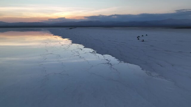 Aerial view of off-road vehicles driving across the vast salt flats of the Danakil Desert during sunset Dalol, Afar, Ethiopia.