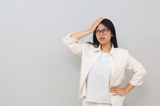 Portrait of an annoyed young Asian girl, slapping her forehead and rolling her eyes upwards in annoyance, forgetting something important, making a mistake, standing on a white background.