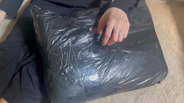 Close up of a woman hands cutting black plastic package wrapper with scissors to unbox a new carpet