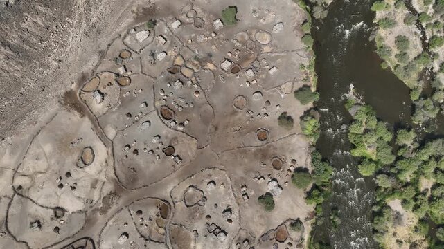 Aerial view of a traditional settlement with circular enclosures and huts located along a winding river with lush green banks in Dallol, Afar, Ethiopia.