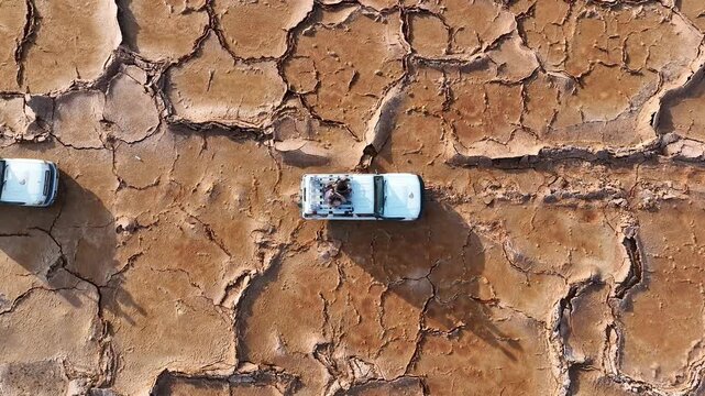 Aerial view of white off-road vehicles driving across the cracked and parched earth of the Danakil Desert Dalol, Afar, Ethiopia.