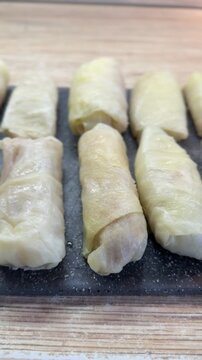 Cabbage rolls on black cutting board closeup, uncooked meat filled cabbage leaves rolled into neat cylinders, arranged in rows