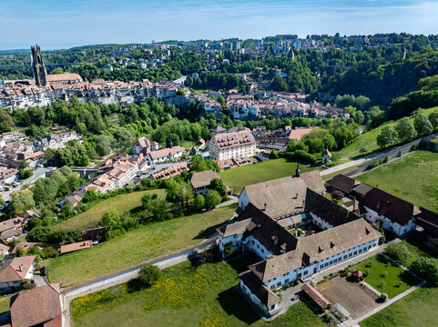Aerial view of Monastere de Montorge surrounded by green meadows with the historic skyline of Fribourg and St. Nicholas Cathedral in the background, Fribourg, Fribourg, Switzerland.