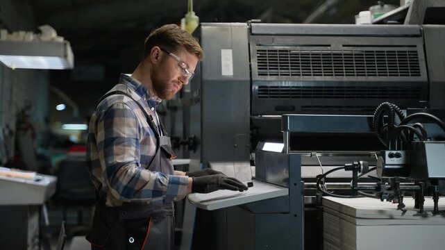 Printing house worker operating industrial offset machine