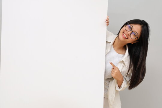 Portrait of a happy and excited young woman, smiling positively, pointing with finger, empty space, plain white billboard, advice, choice, isolated on white background.