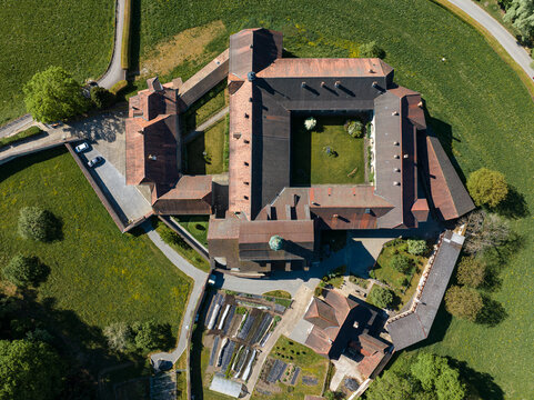 Aerial view of La Maigrauge Abbey featuring historic stone buildings with red-tiled roofs, a central courtyard, and lush green gardens in Fribourg, Fribourg, Switzerland.