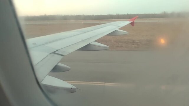 Airplane wing viewed from window during landing approach on runway, showcasing gradual descent and ground proximity with visible landscape in the background