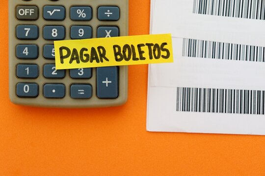 Post-it note with the words "Pagar Boletos" (bill payment, in Portuguese) next to bills with barcodes (c&oacute;digo de barras), computer and a calculator. 