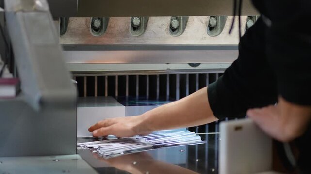 Print shop worker operating industrial guillotine paper cutter machine