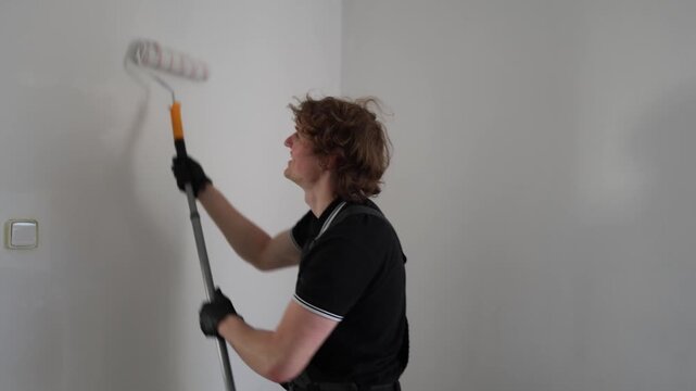 Happy apartment painter enjoying renovation process while rolling fresh white paint on walls in empty room with positive mood and clean modern interior feeling
