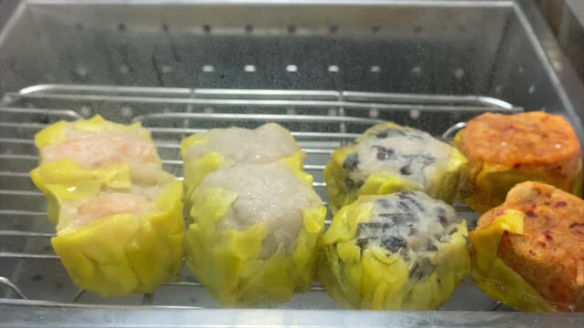 Steamed buns and various dim sum shumai inside a hot glass steamer showcase