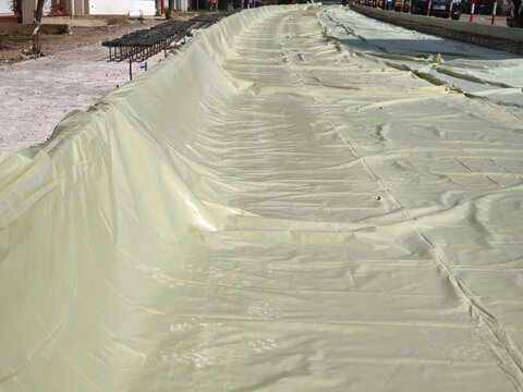 Road construction site with concrete curing plastic sheet covering the ground.