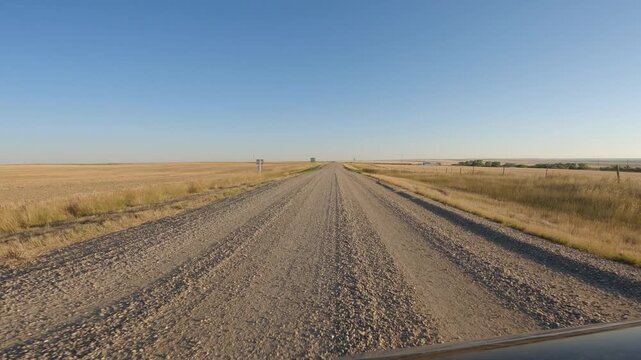 POV driving along a gravel road through a dry prairie landscape and stopping at stop signs

