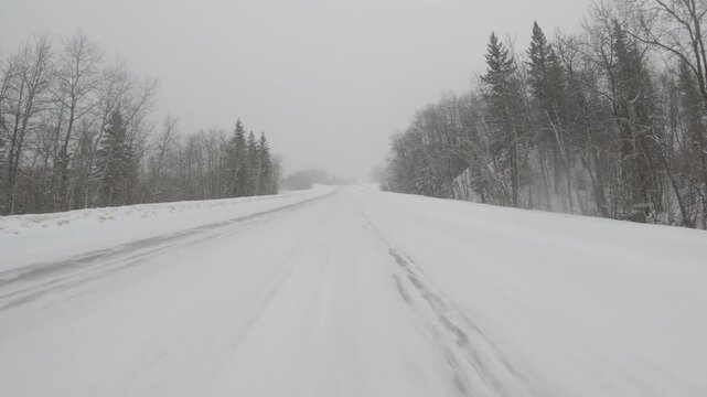 POV from the front of a vehicle driving along a snow covered road during a snow storm. A vehicle passes.
