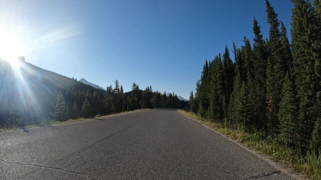 Driving along a northern mountain park road with the sun creating a strong sun-flare on the left side
