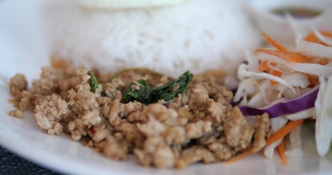 Cinematic close-up of traditional Thai stir-fried minced pork with holy basil (Pad Kra Prow) served with steamed rice, fried egg, and fresh salad on a white plate