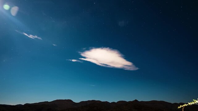 Nocturnal timelapse shows a starry sky and Milky Way hints over Table Mountain, Cape Town. Fast cloud layers sweep overhead, moonlit and city lit, horizon stays sharp.