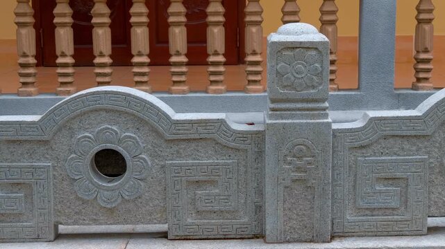 A stone-carved railing in garden of Truc Lam Zen Monastery in Da Lat, Vietnam, composed of posts (watchtowers) and carved panels (wave boards) made from granite with lotus petals carvings
