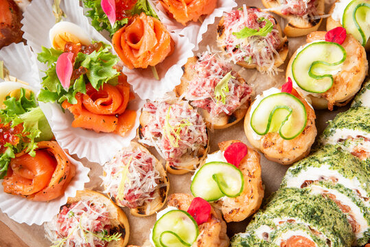 An assortment of elegant catering finger foods, including smoked salmon roses, bruschetta with beef tartare, and cucumber appetizers arranged on a platter.