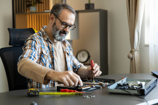 Mature man concentrating on disassembling an electronic device for repair, showcasing diy skills and a hobby for tinkering