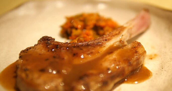 Cinematic close-up of premium grilled bone-in pork chop steak topped with rich gravy sauce, luxury restaurant fine dining gastronomy concept