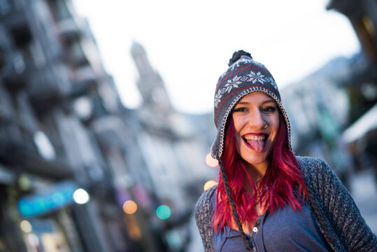 Beautiful woman with piercings sticking out her tongue on a winter day in a European city