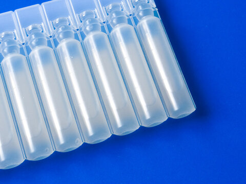 Row of sterile plastic liquid ampoules on blue background, pharmaceutical unit-dose vials for oral or respiratory treatment, medical solution containers