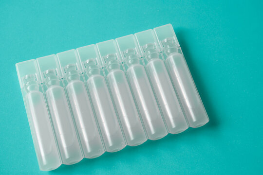 Row of sterile plastic liquid ampoules on green background, pharmaceutical unit-dose vials for medical treatment, liquid medication containers