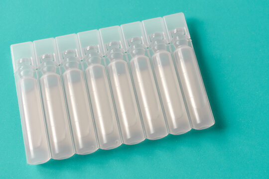 Row of sterile plastic liquid ampoules on green background, pharmaceutical unit-dose vials for medical treatment, liquid medication containers