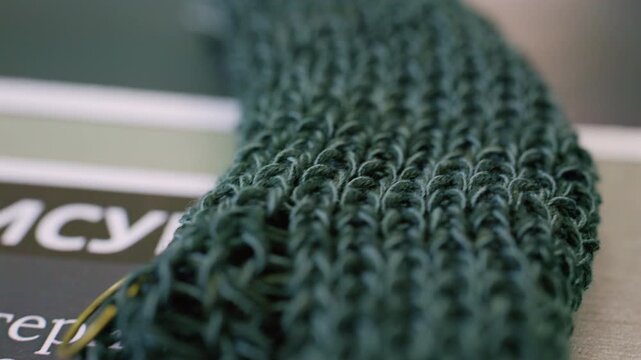 Close up of dark green knitted fabric with large textured loops and visible gold stitch markers