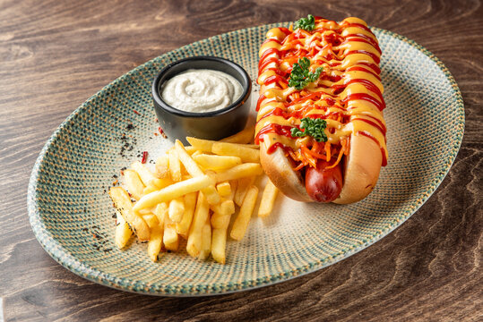 Gourmet hot dog with french fries and sauce on a plate.