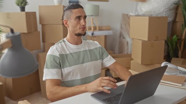 Man with finger to temple by laptop among moving boxes in new home surrounded by stacked cardboard boxes and lamp; thoughtful planning.