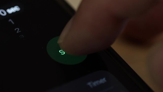 Macro 4K view of a finger pressing a green "Start" button on a black screen, activating the countdown timer or video play feature.