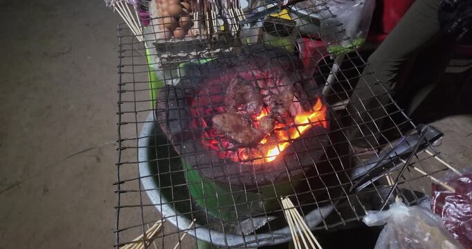 slow motion of close up of meat grilling over bright orange flames on a traditional charcoal stove with a wire grill at night.