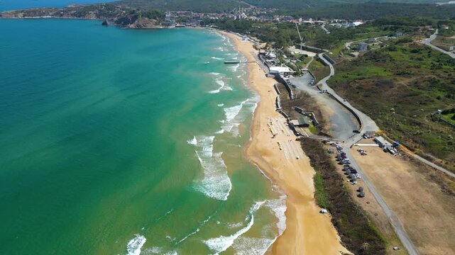Scenic aerial follow shot tracking a beautiful rocky coastline and a sharp cliff headland bordering crystal clear turquoise ocean water with rolling white sea waves during summertime